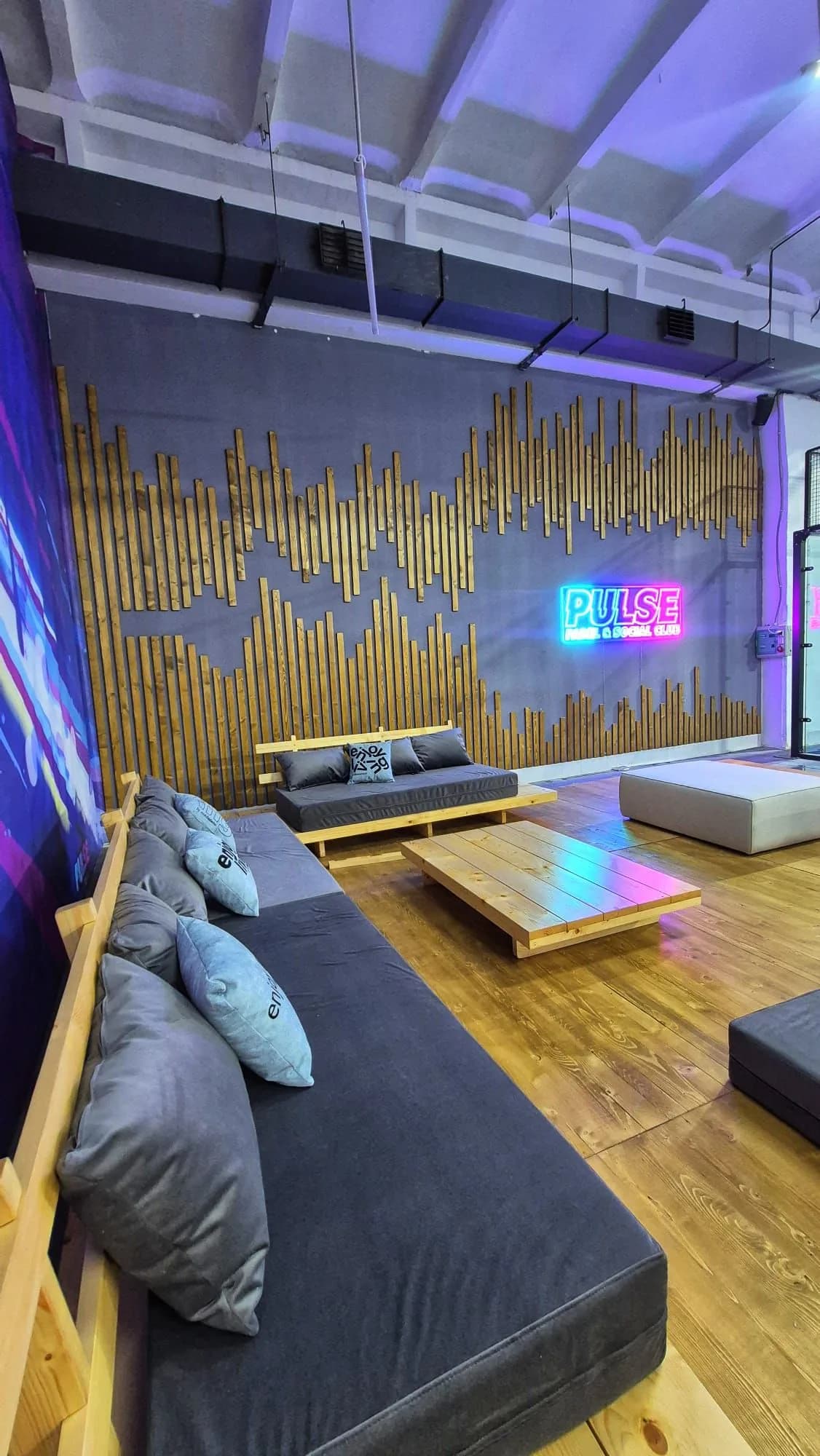 Lounge cu canapele, perne și logo PULSE neon pe perete